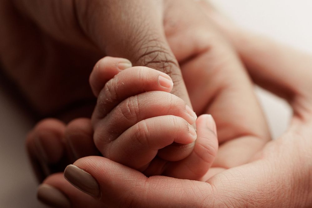 Delicate newborn fingers wrapped around adult hand in intimate close-up photograph.