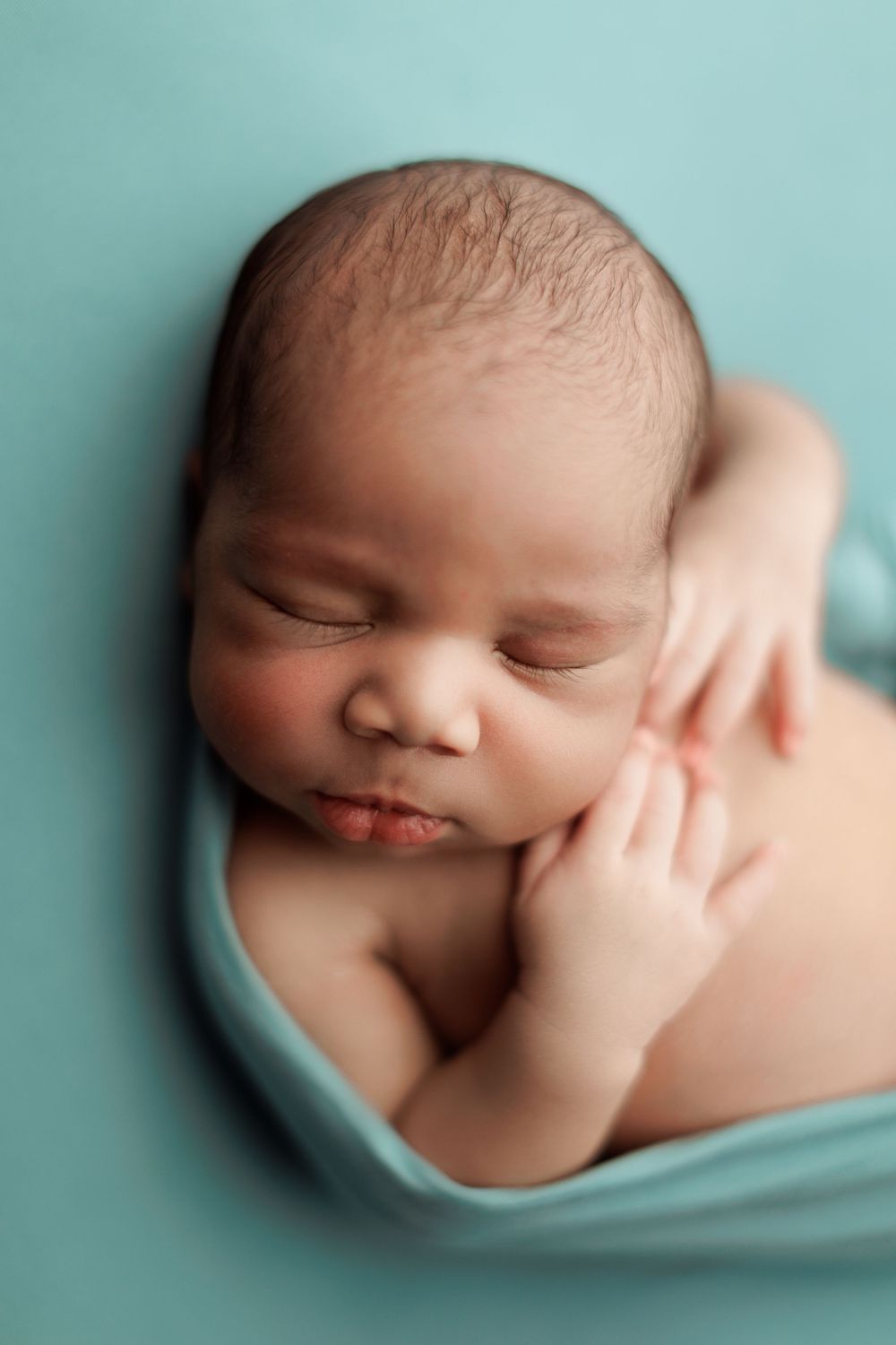 Peaceful sleeping baby wrapped in teal fabric during portrait session.