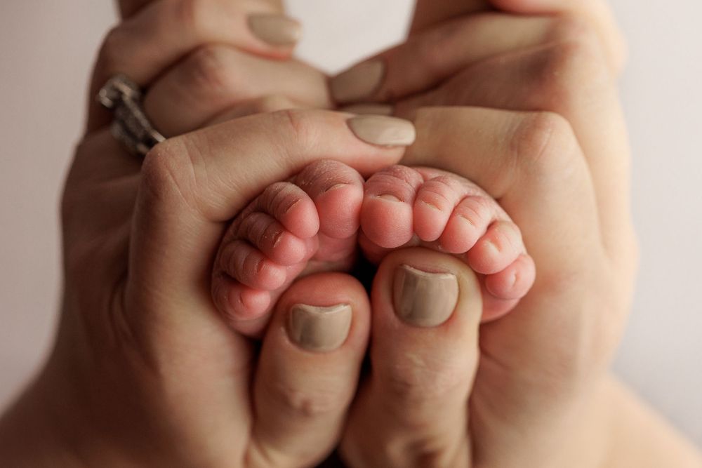 Adult hands gently holding tiny newborn feet with pink toes.