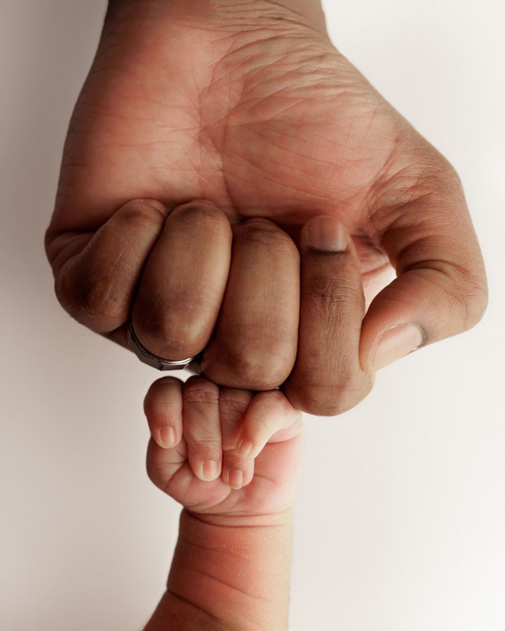 Adult hand gently holding tiny baby finger in artistic black and white portrait.