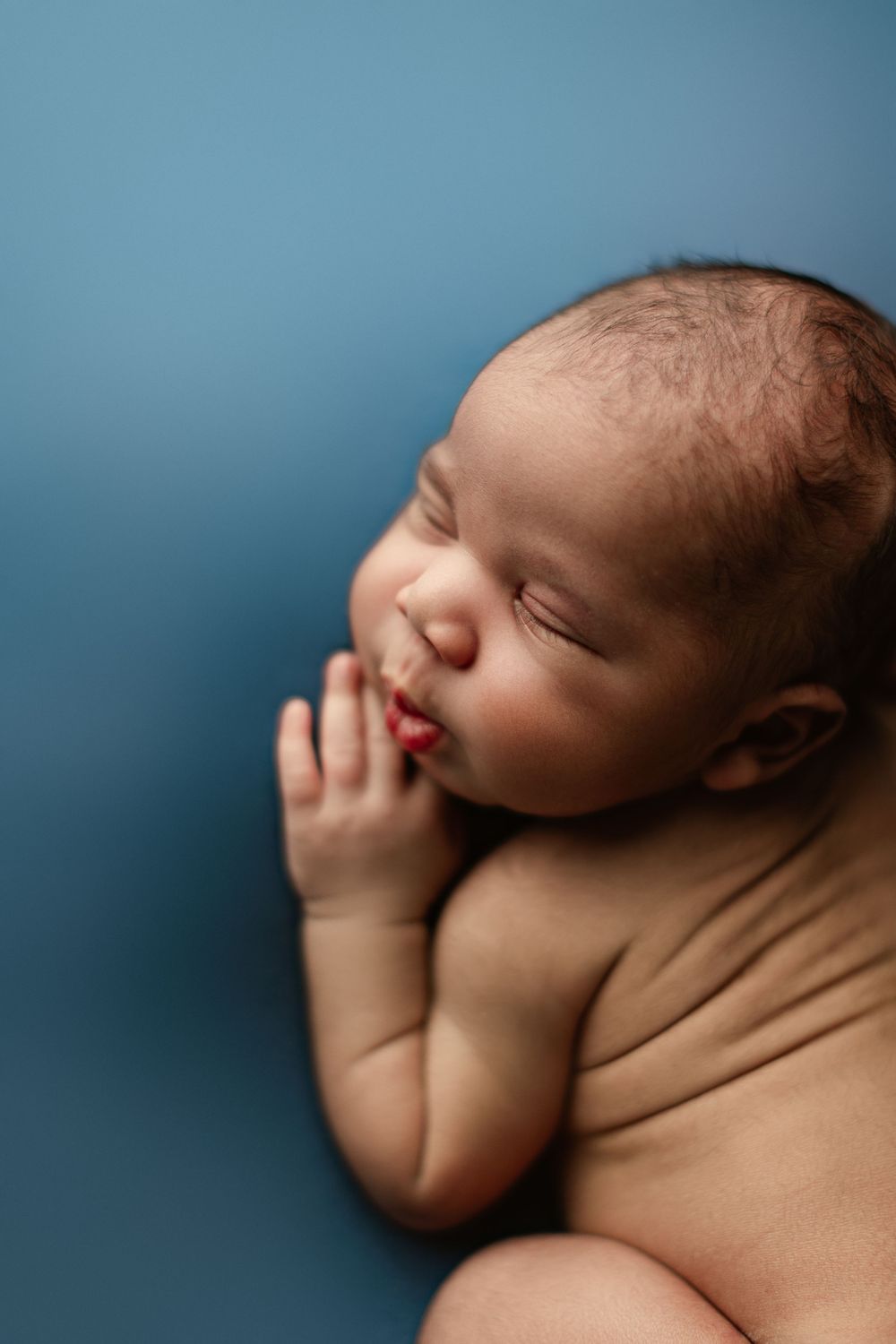 Close-up of sleeping newborn with hand near face against blue background.