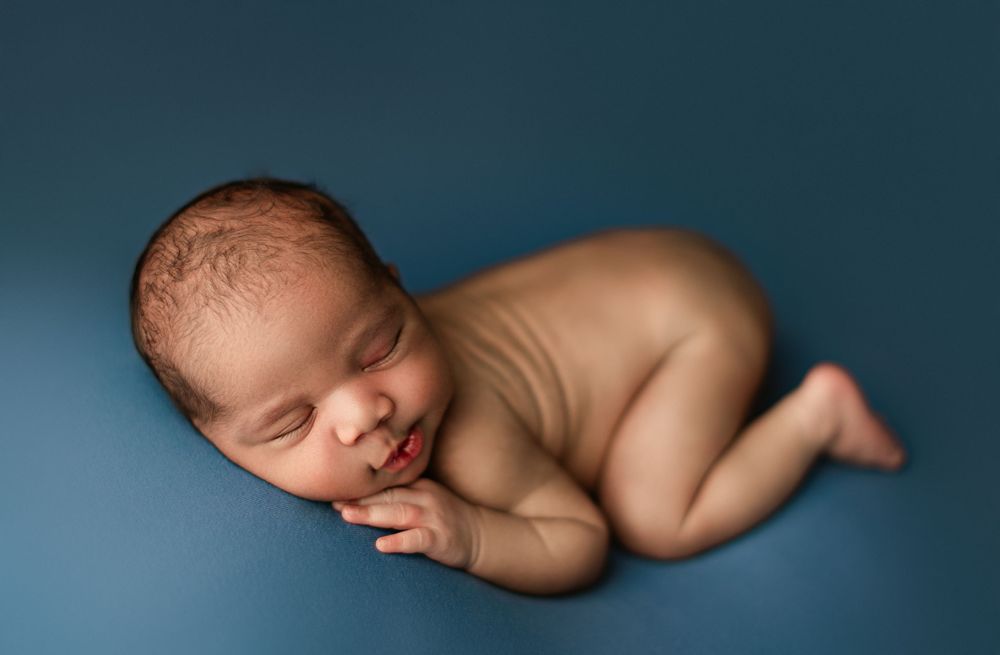 Peaceful sleeping newborn posed on side against dark blue background.
