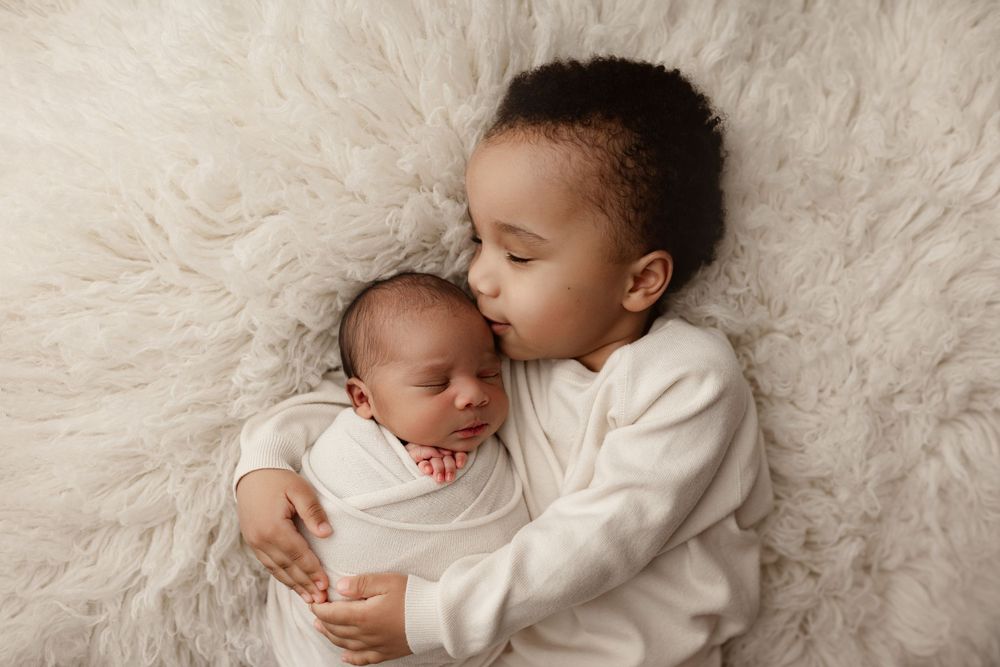 Sweet siblings cuddling on soft white fur backdrop in studio portrait.