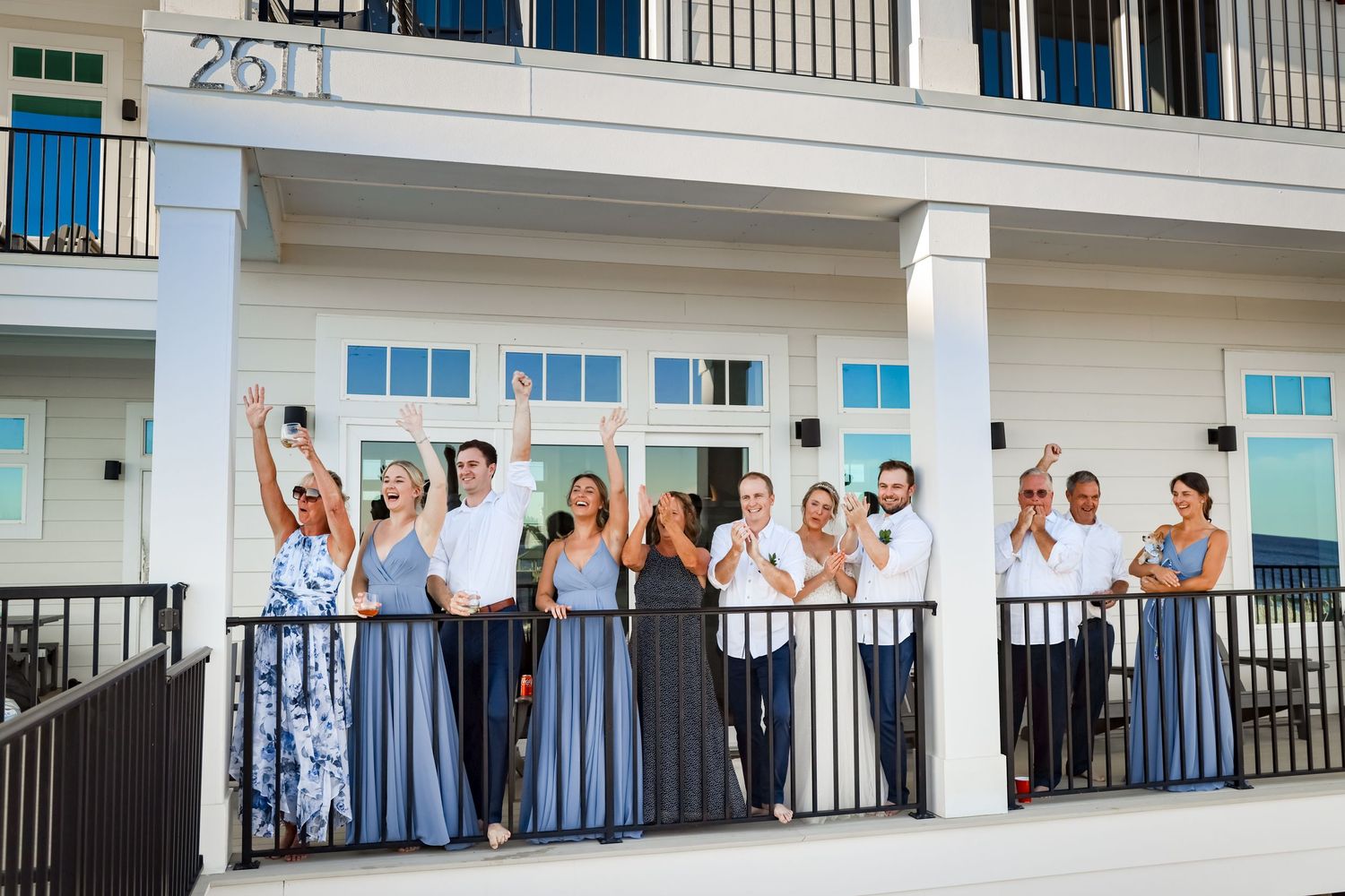 Wedding party in blue dresses poses on white balcony of coastal building.