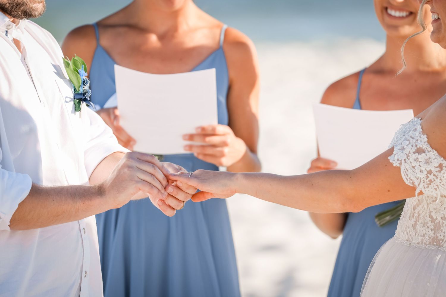 Close-up of hands exchanging rings during beach wedding ceremony.
