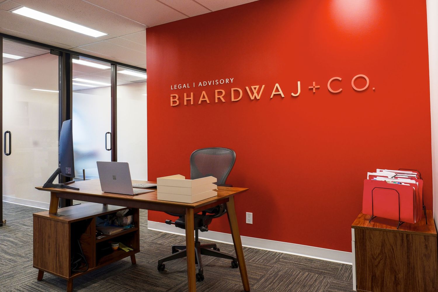 Corporate office space with wooden desk and Bhardwaj + Co branding on red wall.
