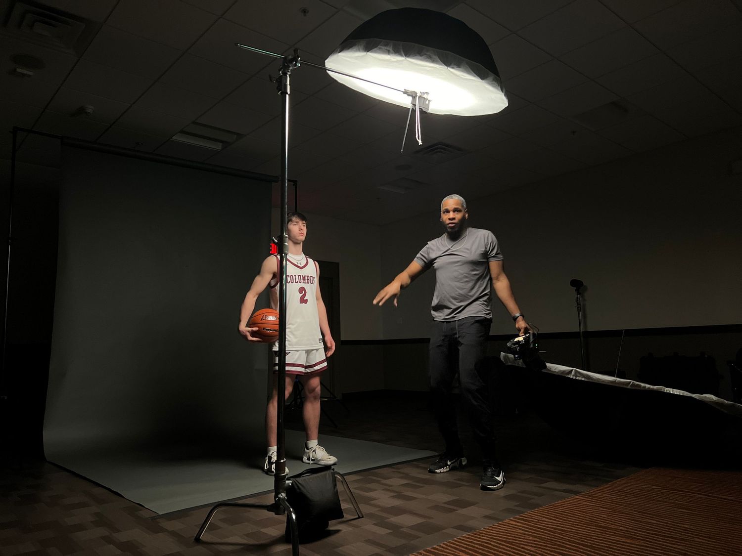 Photography studio setup with lighting equipment and two people positioning for a shot.
