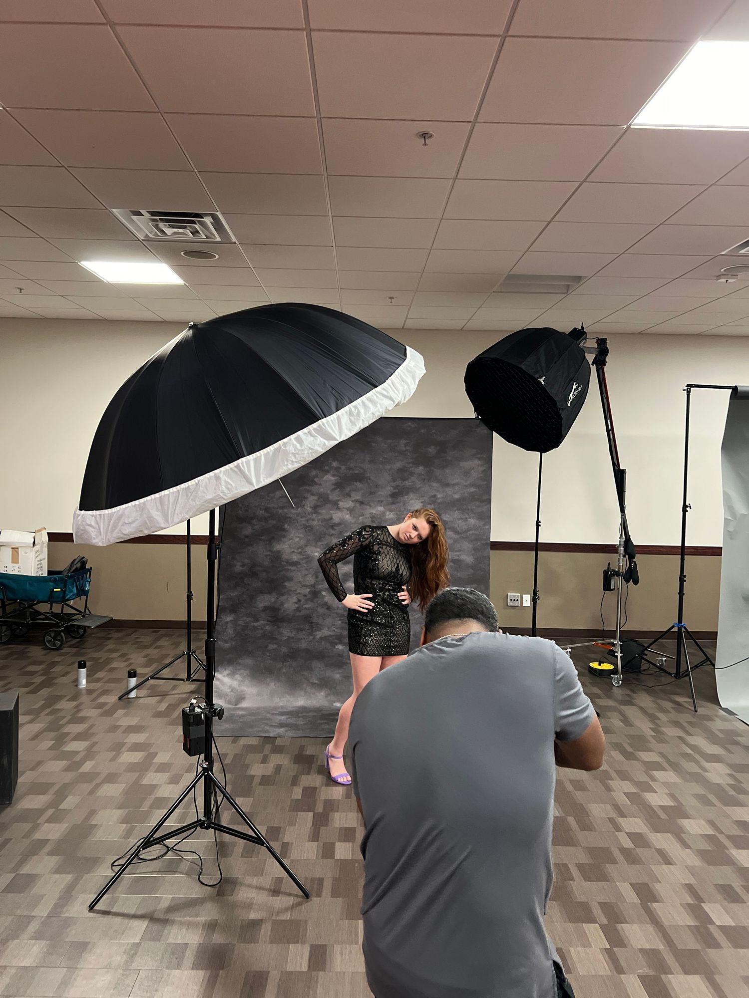 Professional photo shoot setup with large umbrellas and dark backdrop in studio setting.