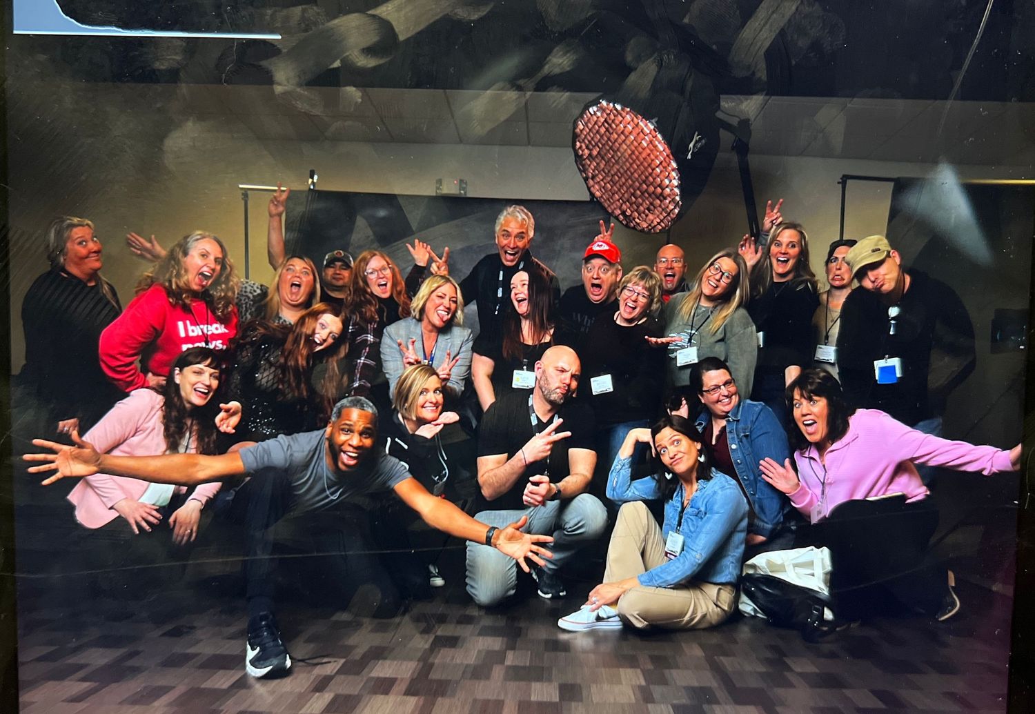 A large group poses together in a dark studio space with dramatic lighting and playful expressions.
