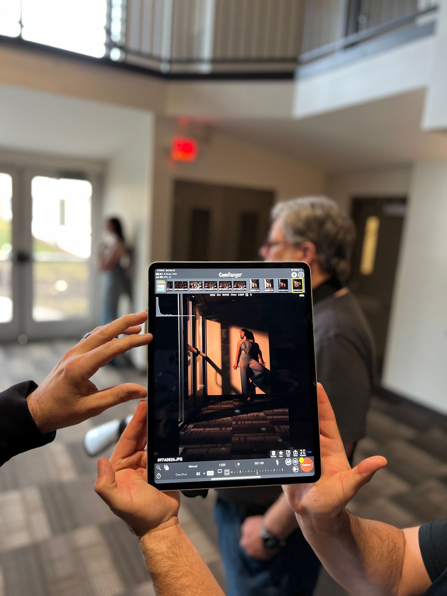 Hands hold up a tablet displaying a photo editing interface with a dark corridor image.