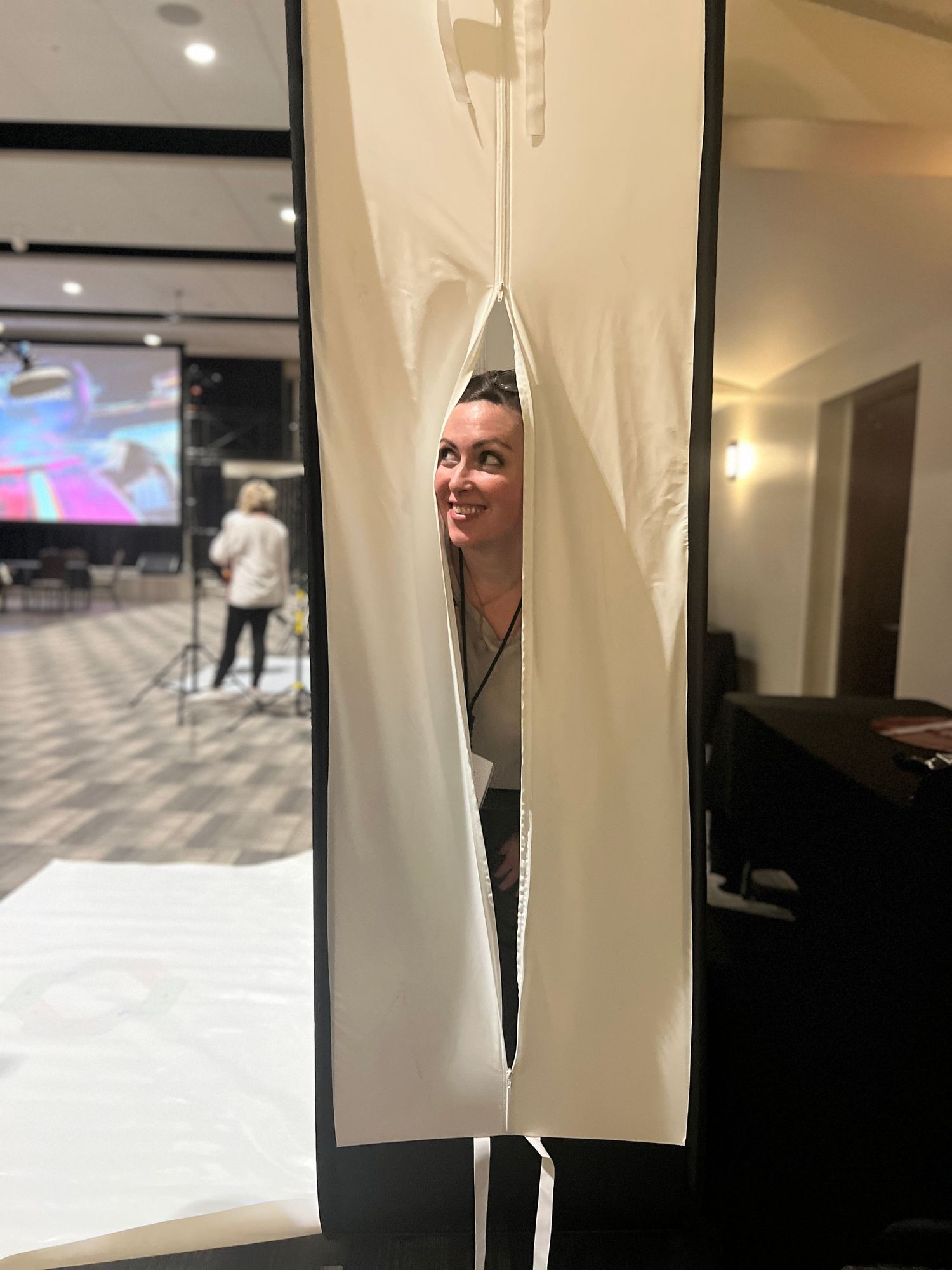 Someone peeks playfully through a split in a white curtain in an indoor space.