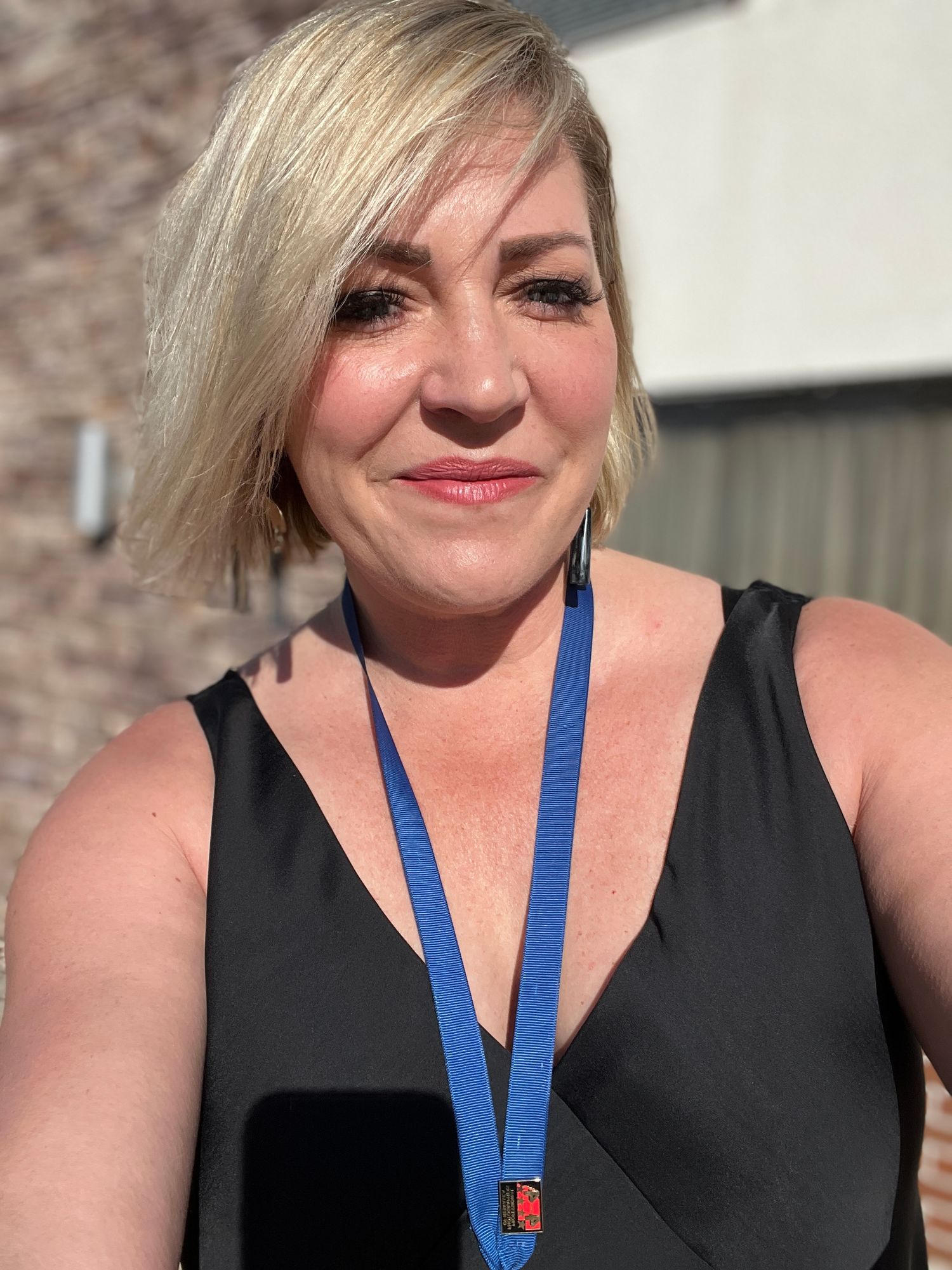 A close-up portrait in sunlight showing a black tank top and blue lanyard.