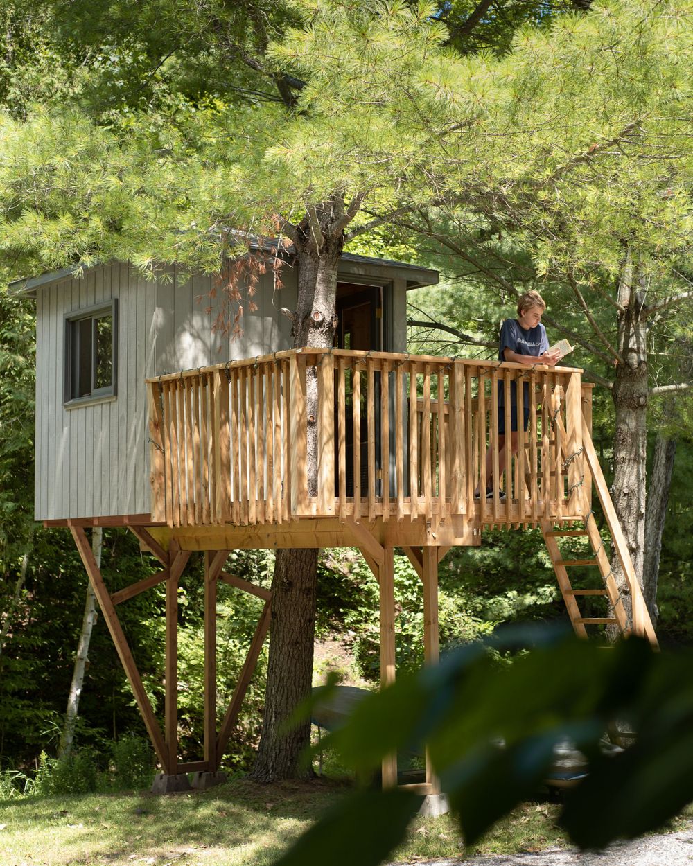 Wooden treehouse with deck and railing built among trees in summer forest.