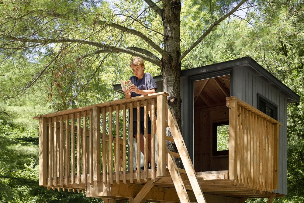 Rustic wooden treehouse with railing and stairs nestled among green trees.