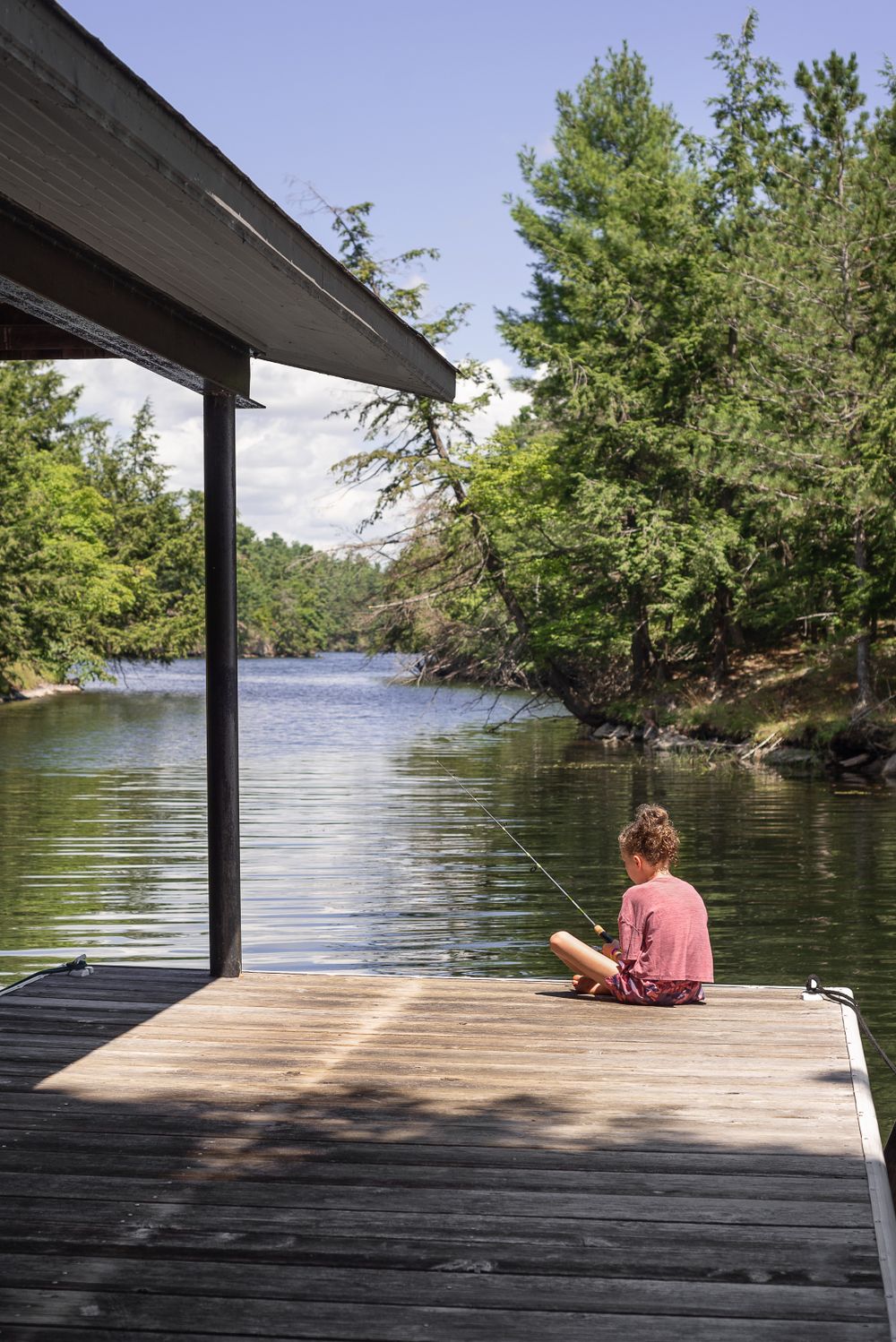 Person sitting alone on wooden dock overlooking peaceful lake surrounded by trees.
