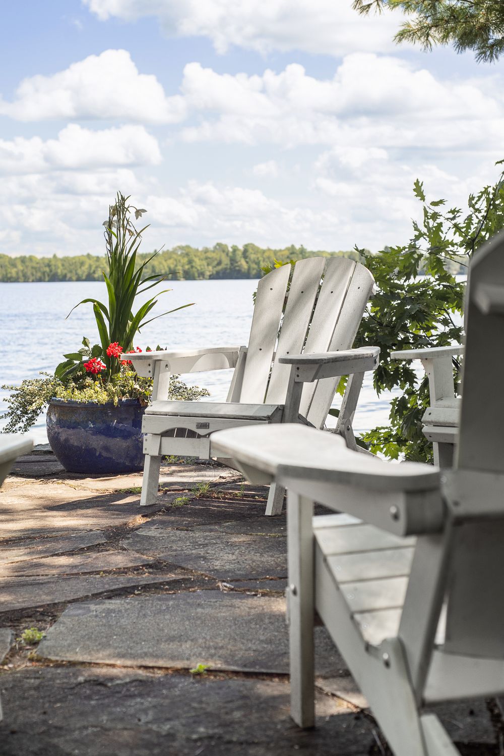 White Adirondack chairs and potted flowers on a lakeside dock with water views.