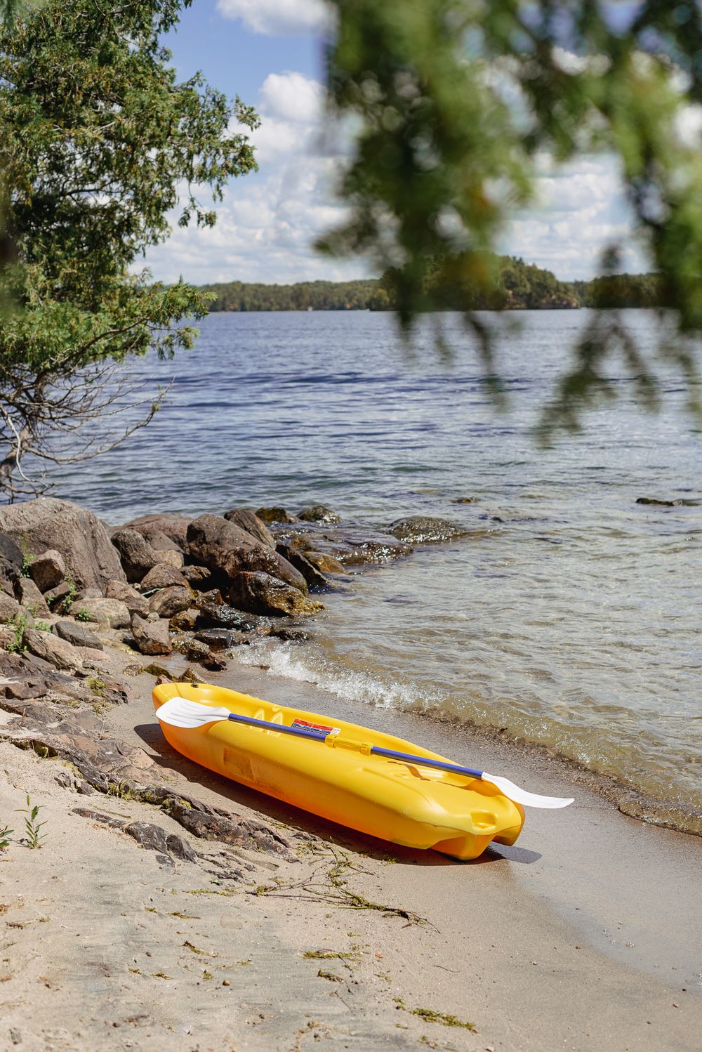 Yellow kayak resting on rocky beach shore with lake and trees in background.
