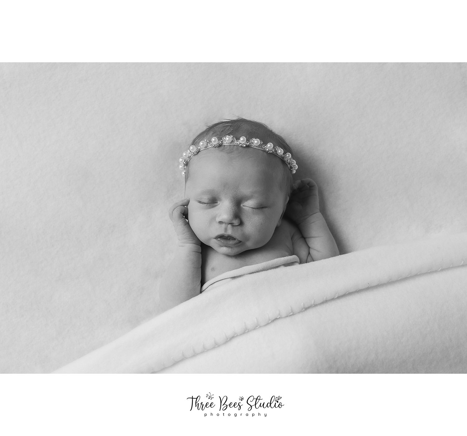 Black and white portrait of sleeping newborn wearing delicate pearl headband.