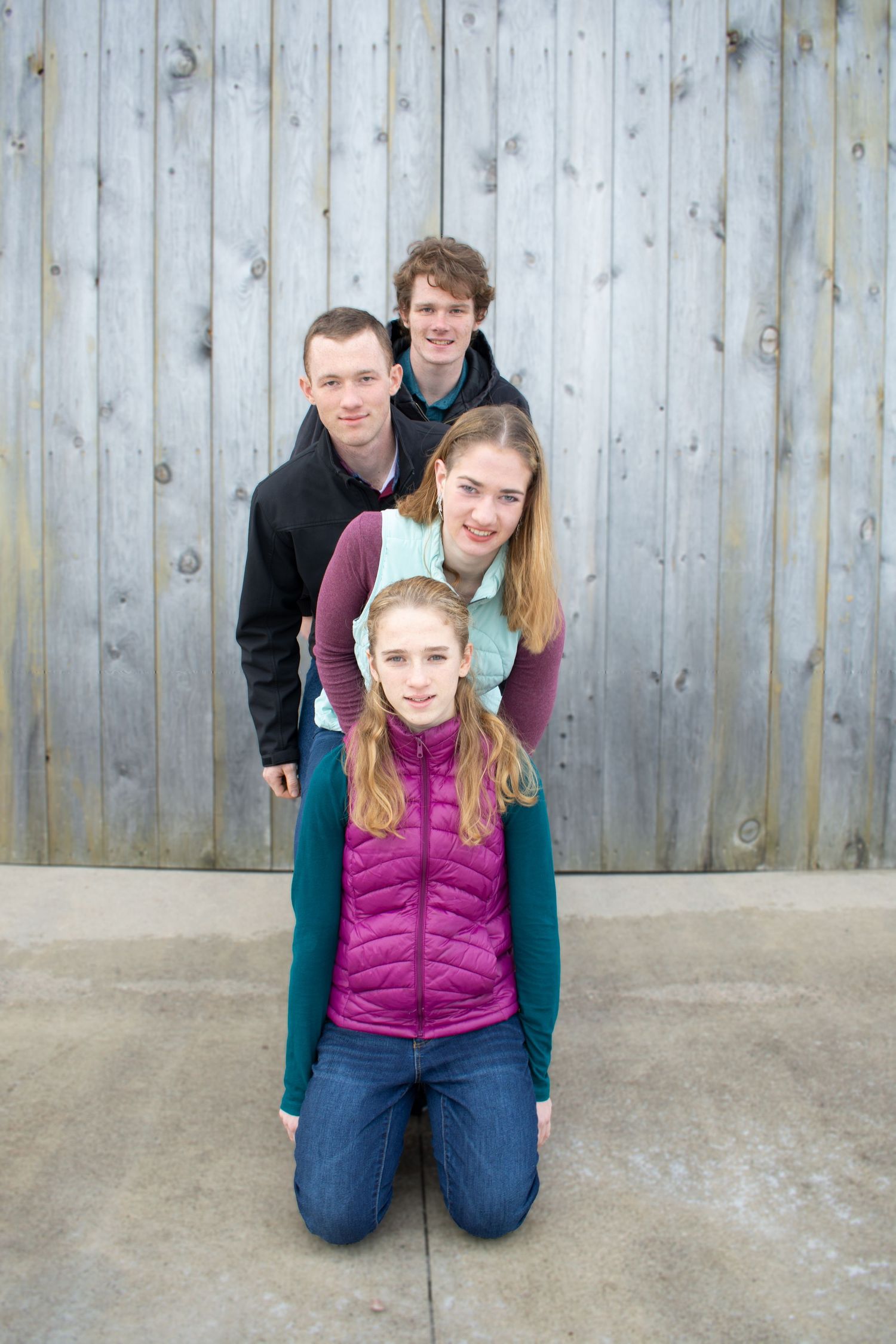 Group photo against weathered wood wall with people stacked in playful poses.