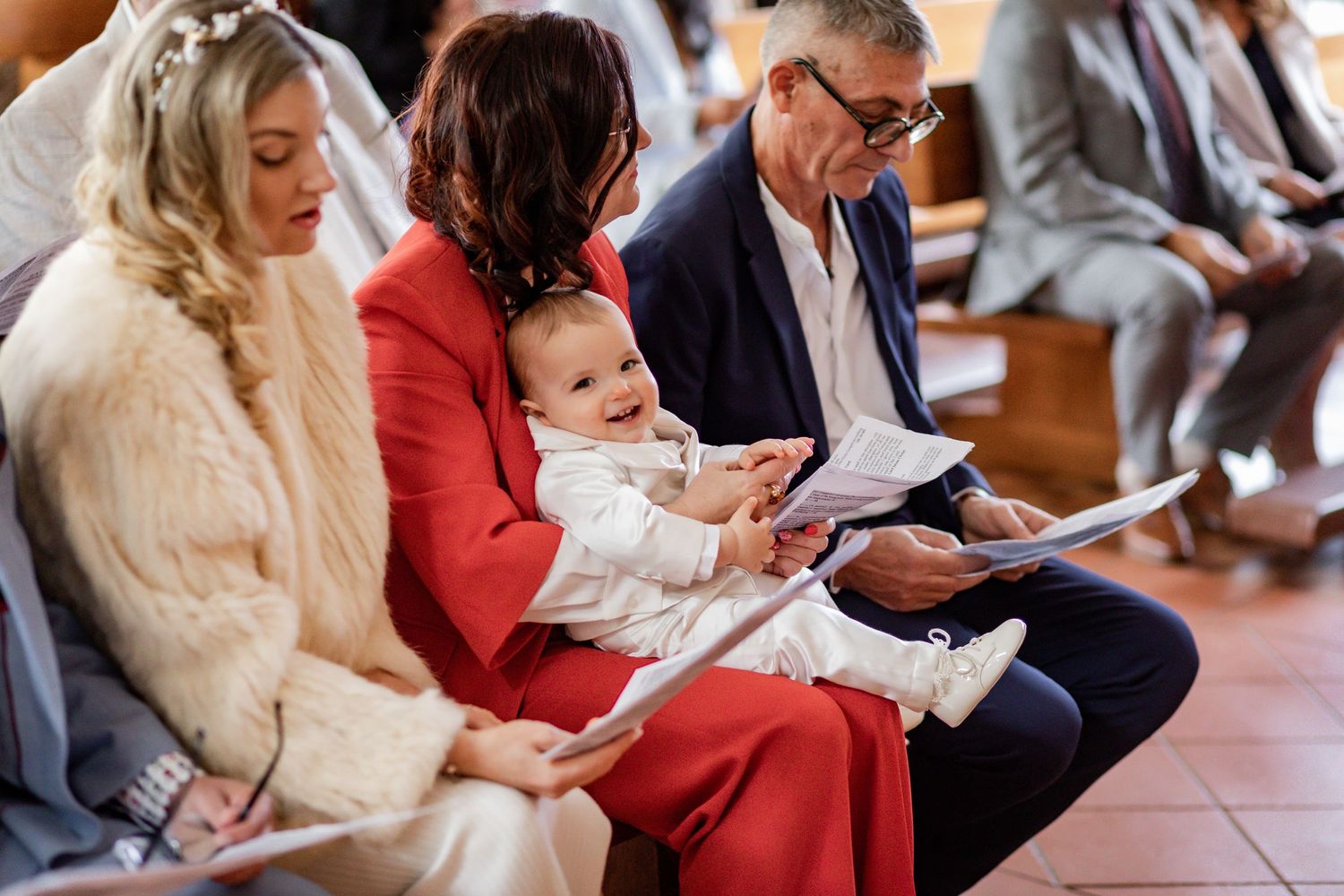 A family attends a church service with a baby wearing white baptismal clothing.