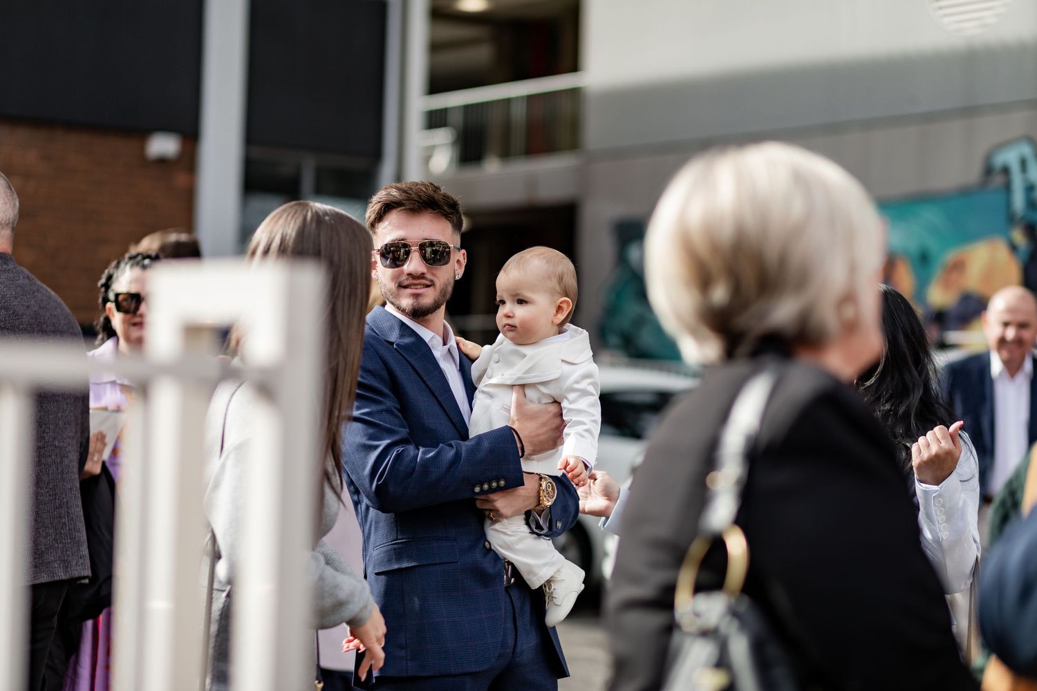 A gathering of people at an outdoor event with someone holding a baby.