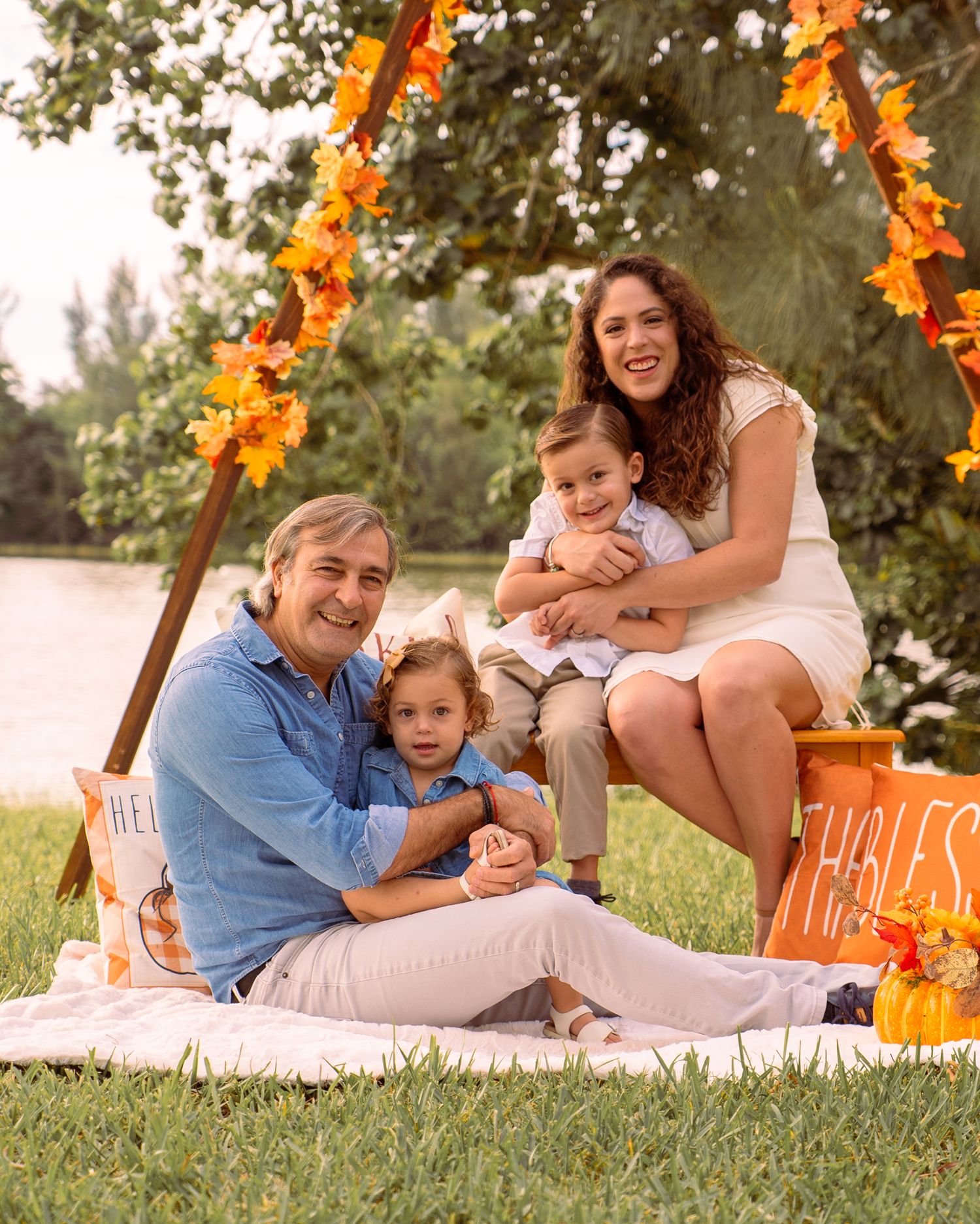Happy family of four poses under autumn leaf arch by lakeside park.