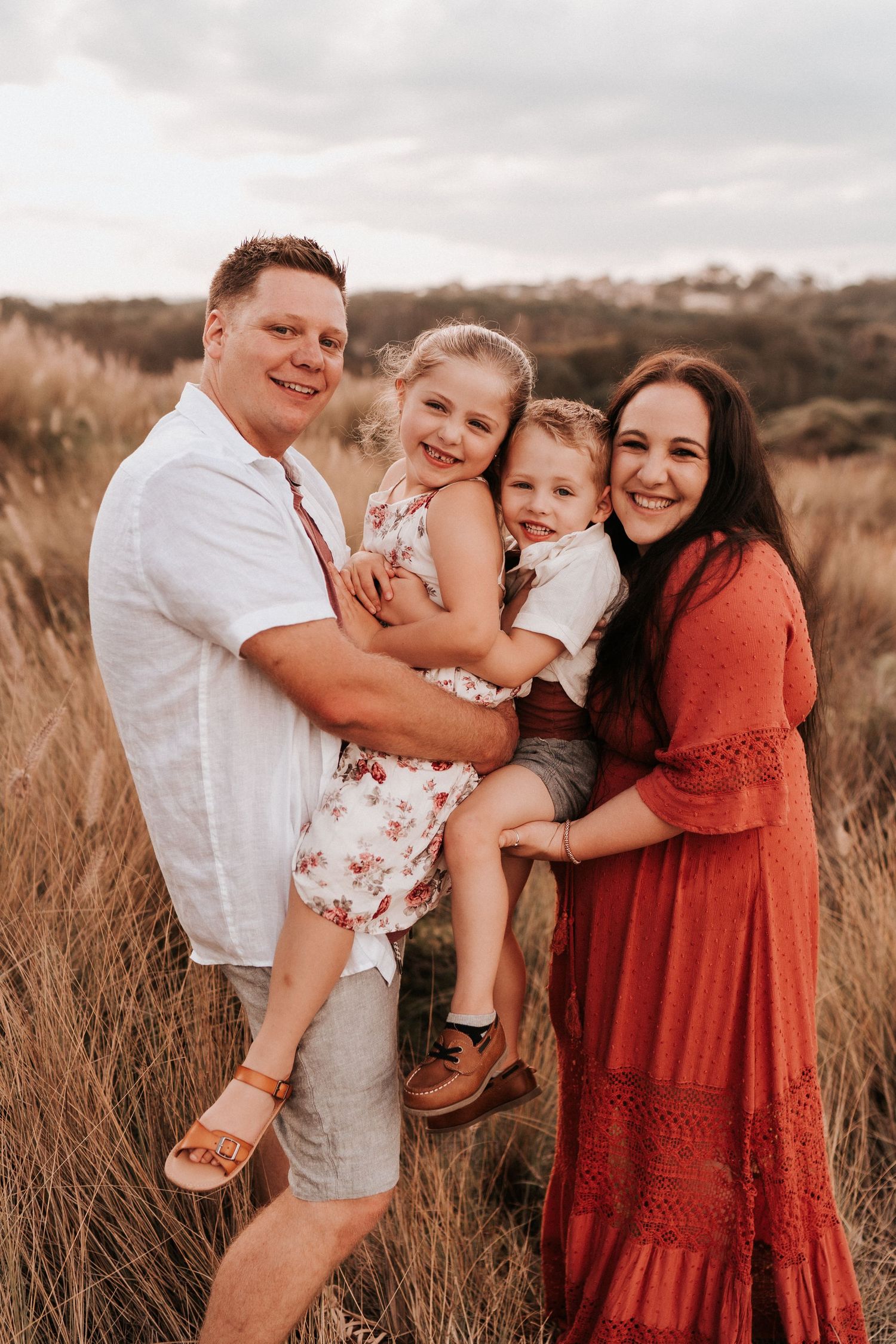 Family playing and laughing together in tall grass during golden hour.