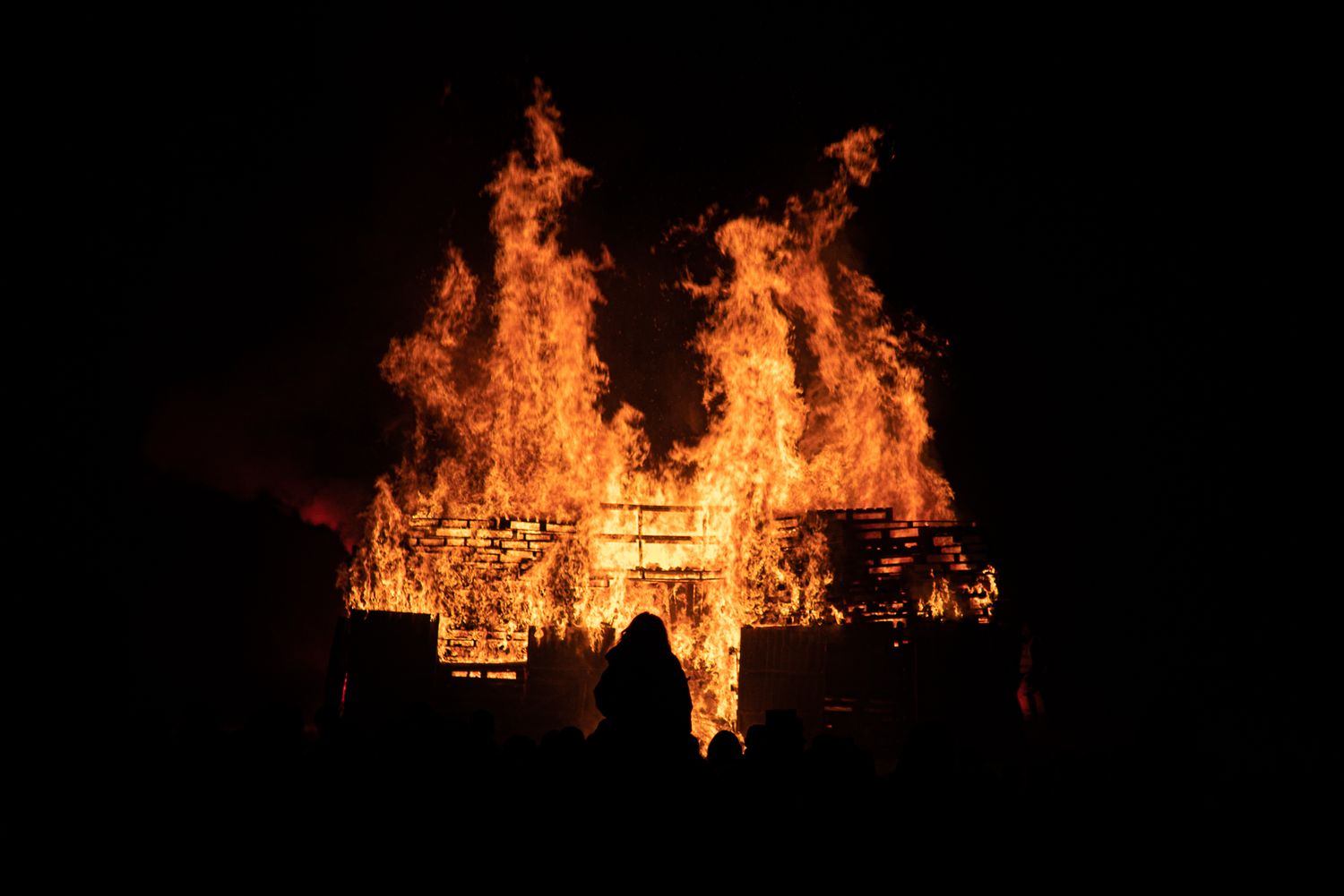 Dramatic nighttime image of a structure engulfed in intense flames.