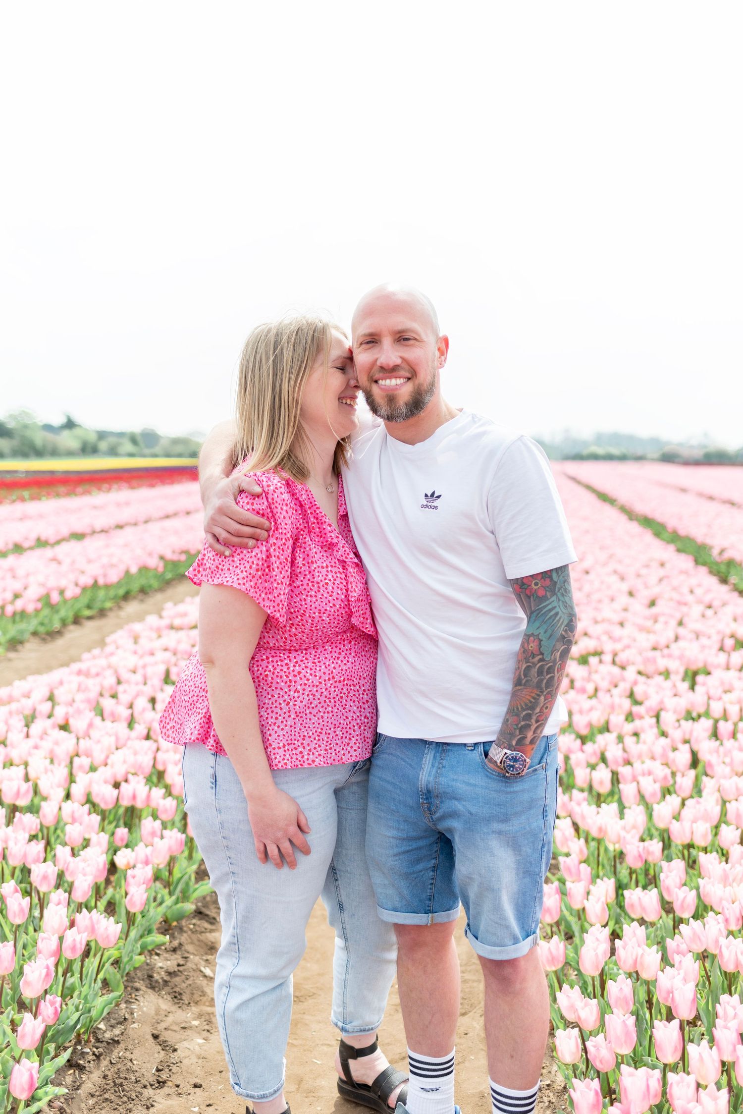 Happy couple posing together in a blooming pink tulip field on a bright spring day.