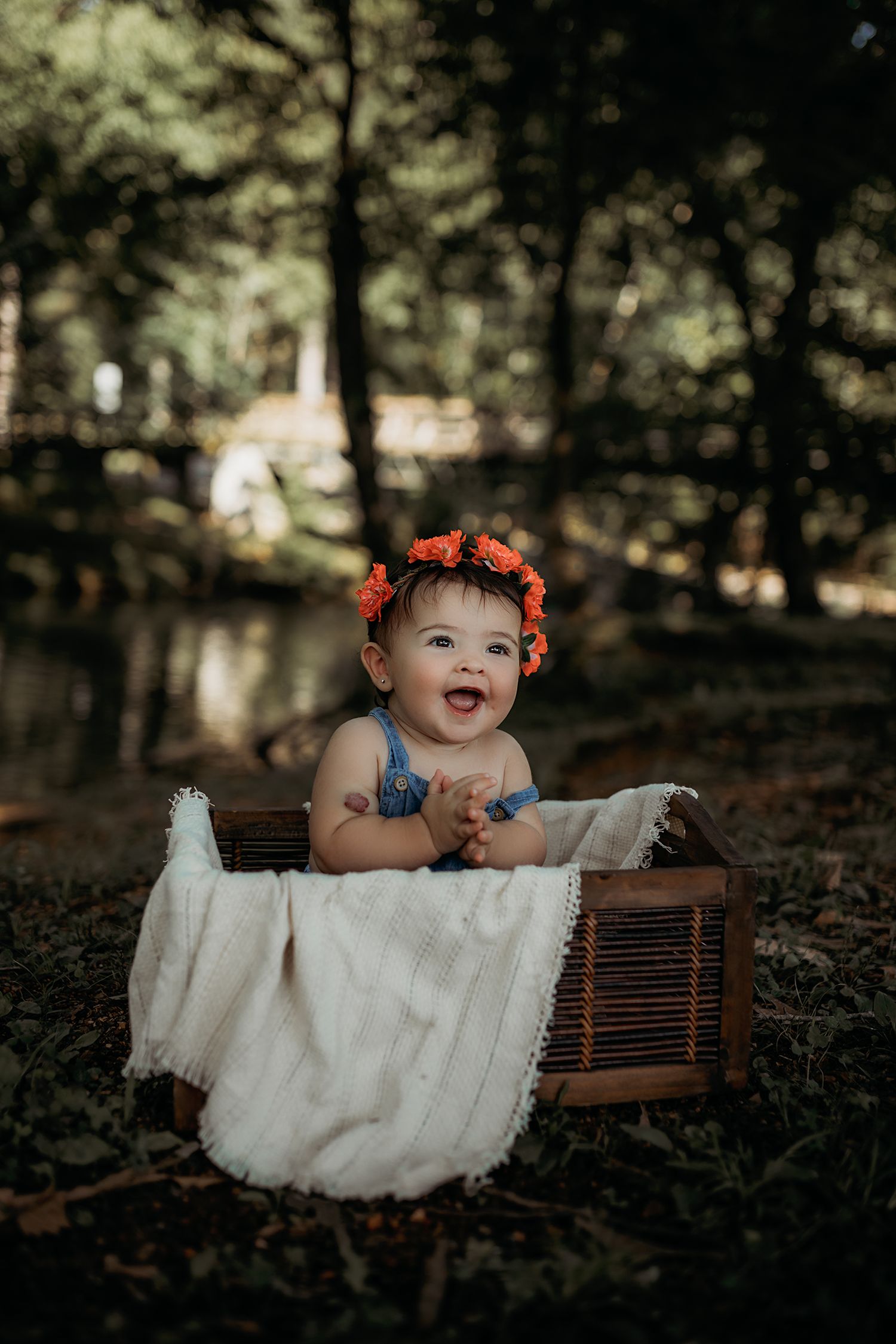 Baby in blue outfit and orange flower crown poses on vintage wooden radio in outdoor setting.