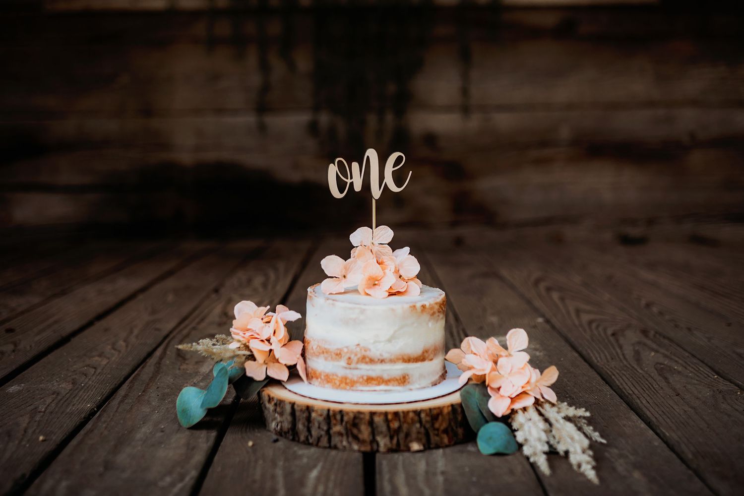 Rustic wooden backdrop with 'one' text and floral decorations for a cake smash photo session.