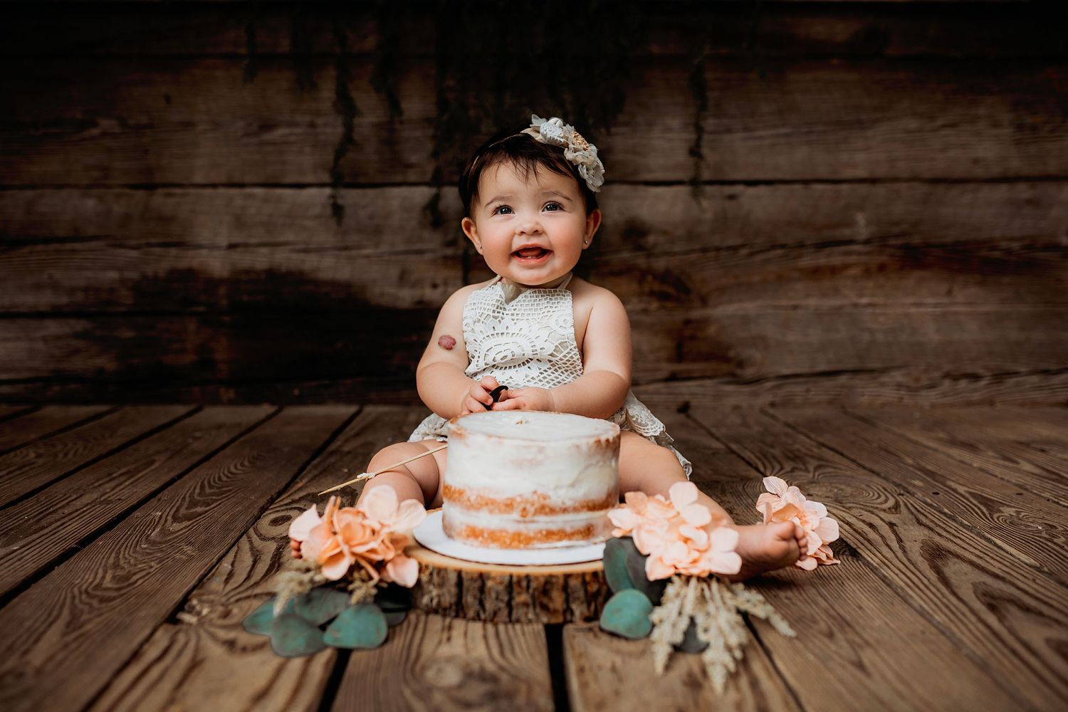First birthday cake smash scene with vintage decorations on wooden floor.