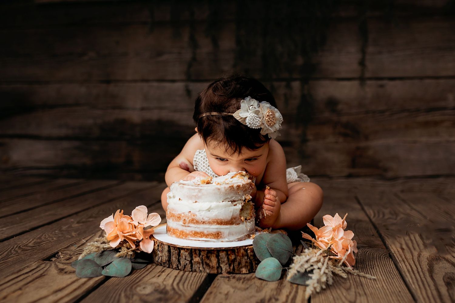 Rustic cake smash setup with floral decorations on dark wooden floor.