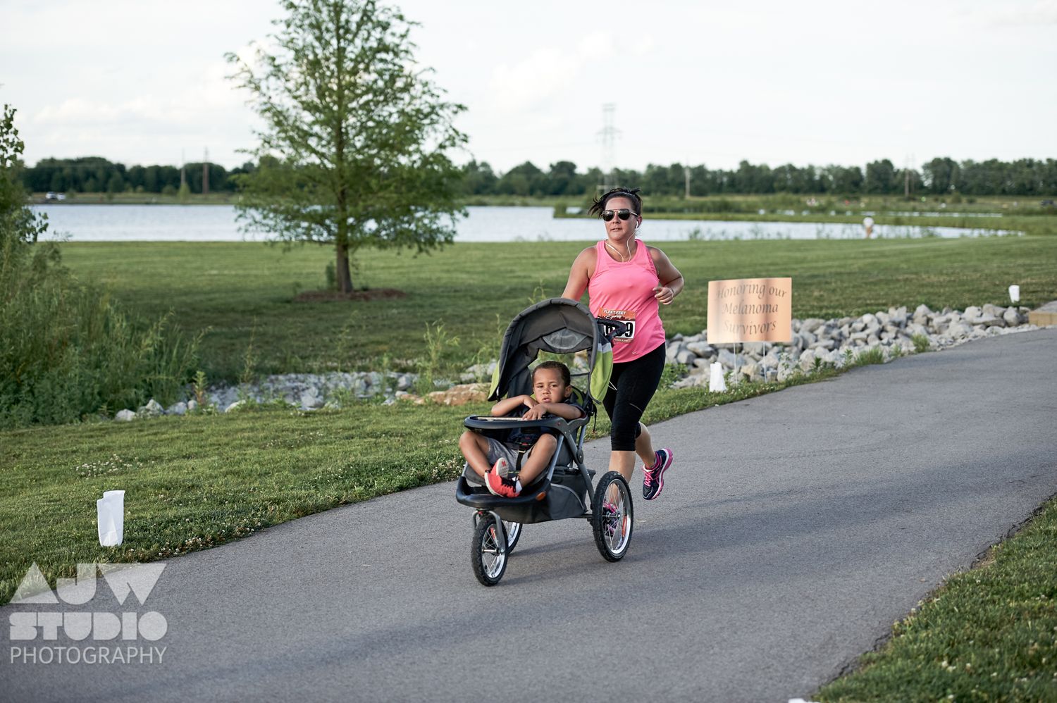 Runner pushing a jogging stroller along a lakeside path during a race event.