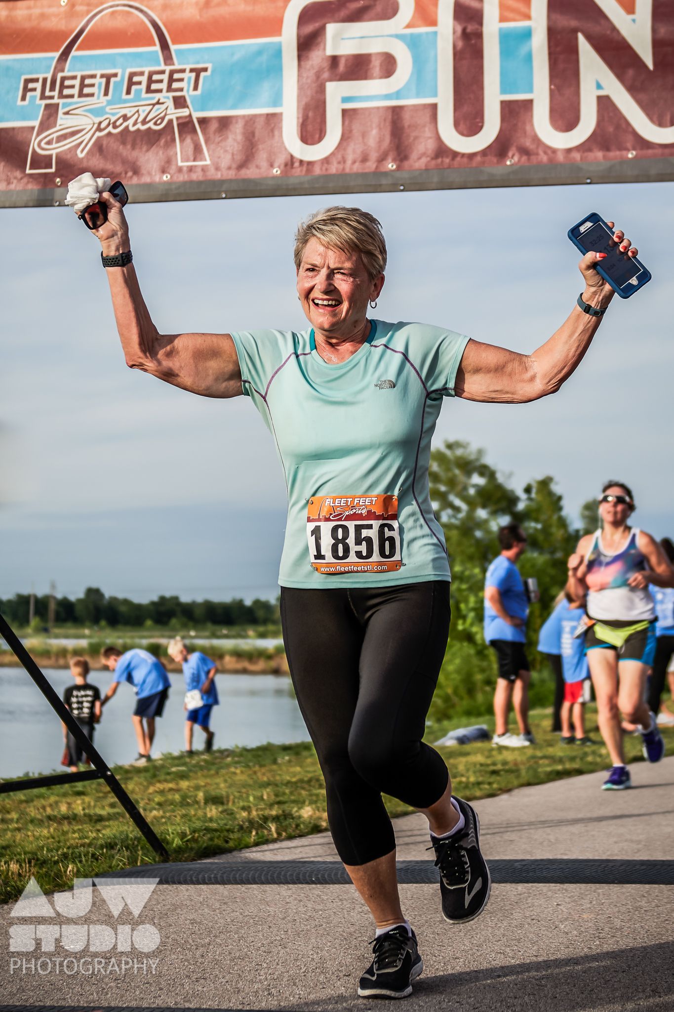 Enthusiastic participant celebrating under Fleet Feet Fun Run banner during lakeside running event.