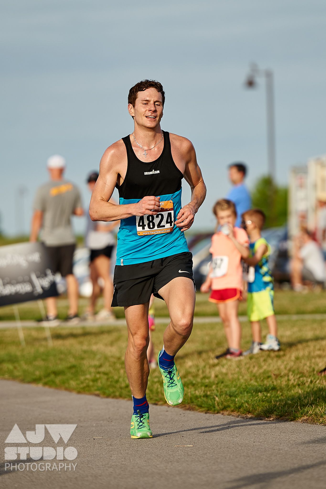 Runner in blue tank top and black shorts runs along waterfront path during race.