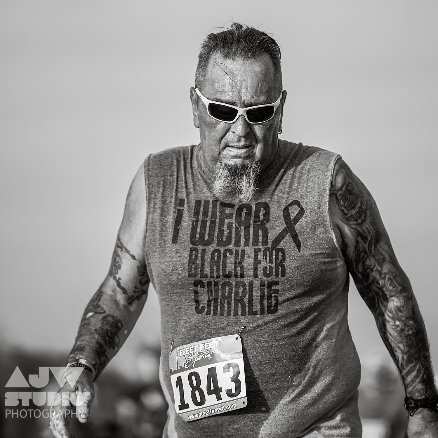 Black and white portrait of runner wearing sunglasses and race bib during event.