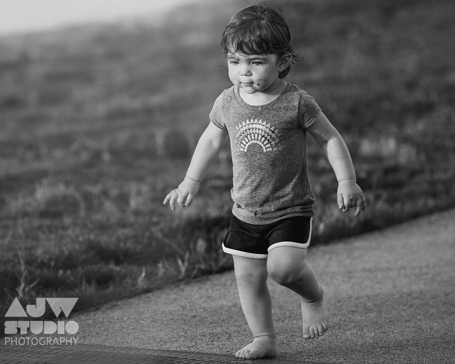 Black and white photo of small child running on outdoor path.