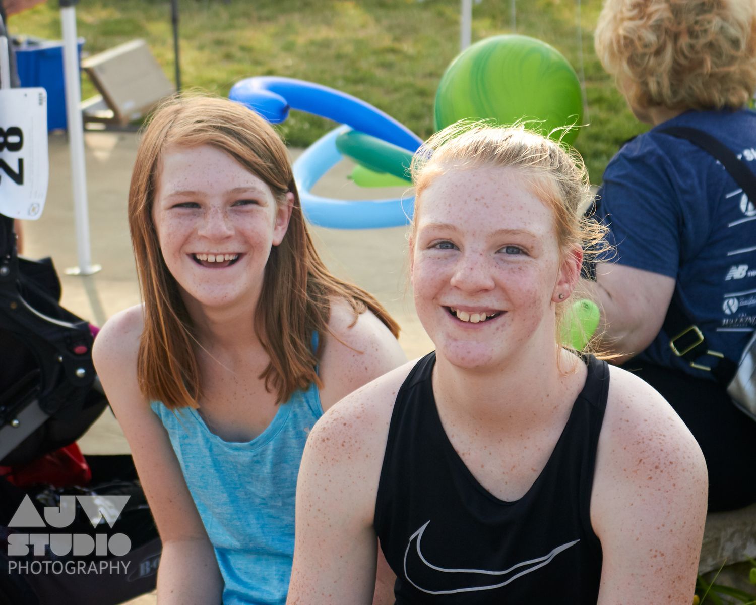 Two runners smiling and enjoying post-race festivities with green balloons in background.