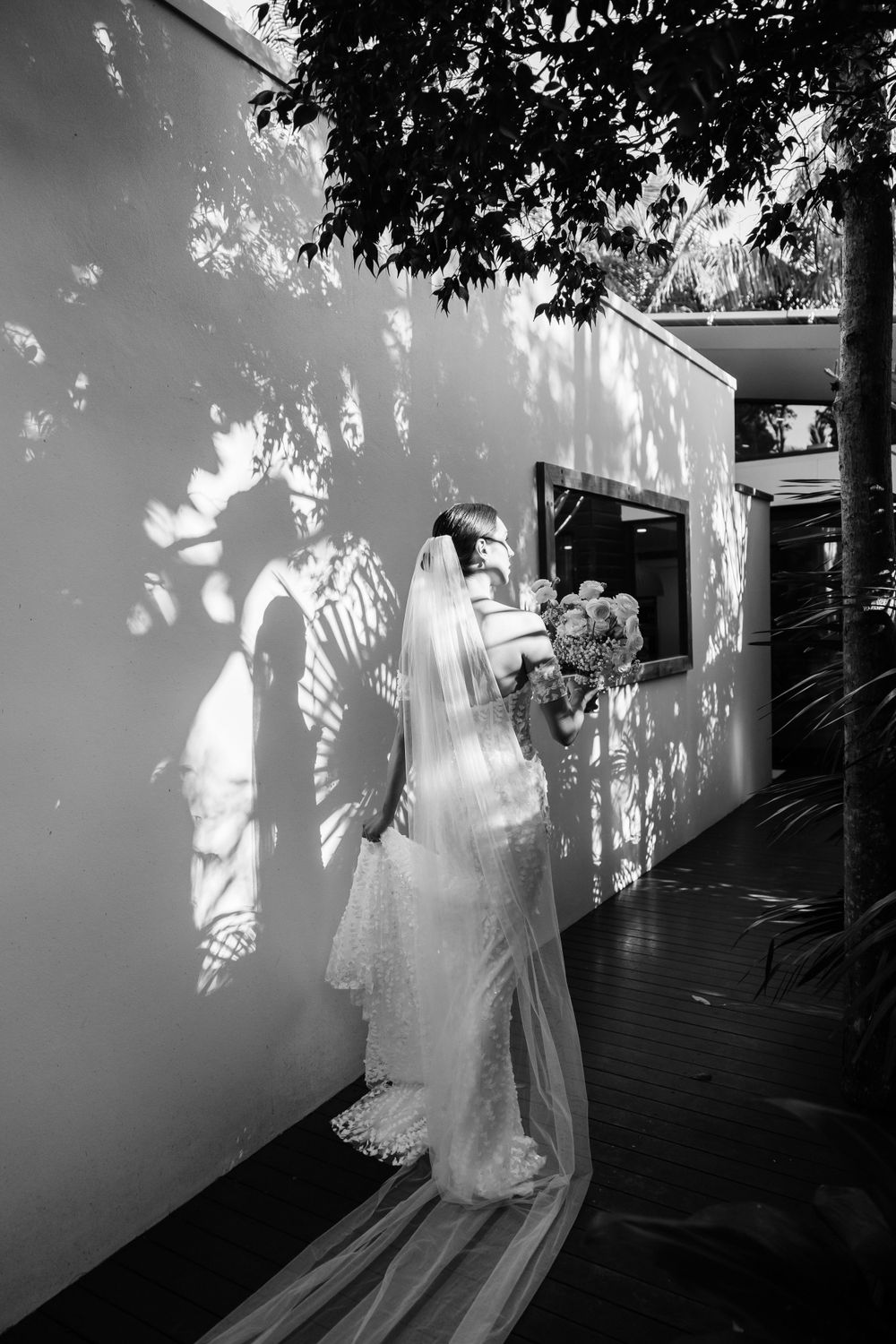 A dramatic black and white wedding photo with dappled light through trees.