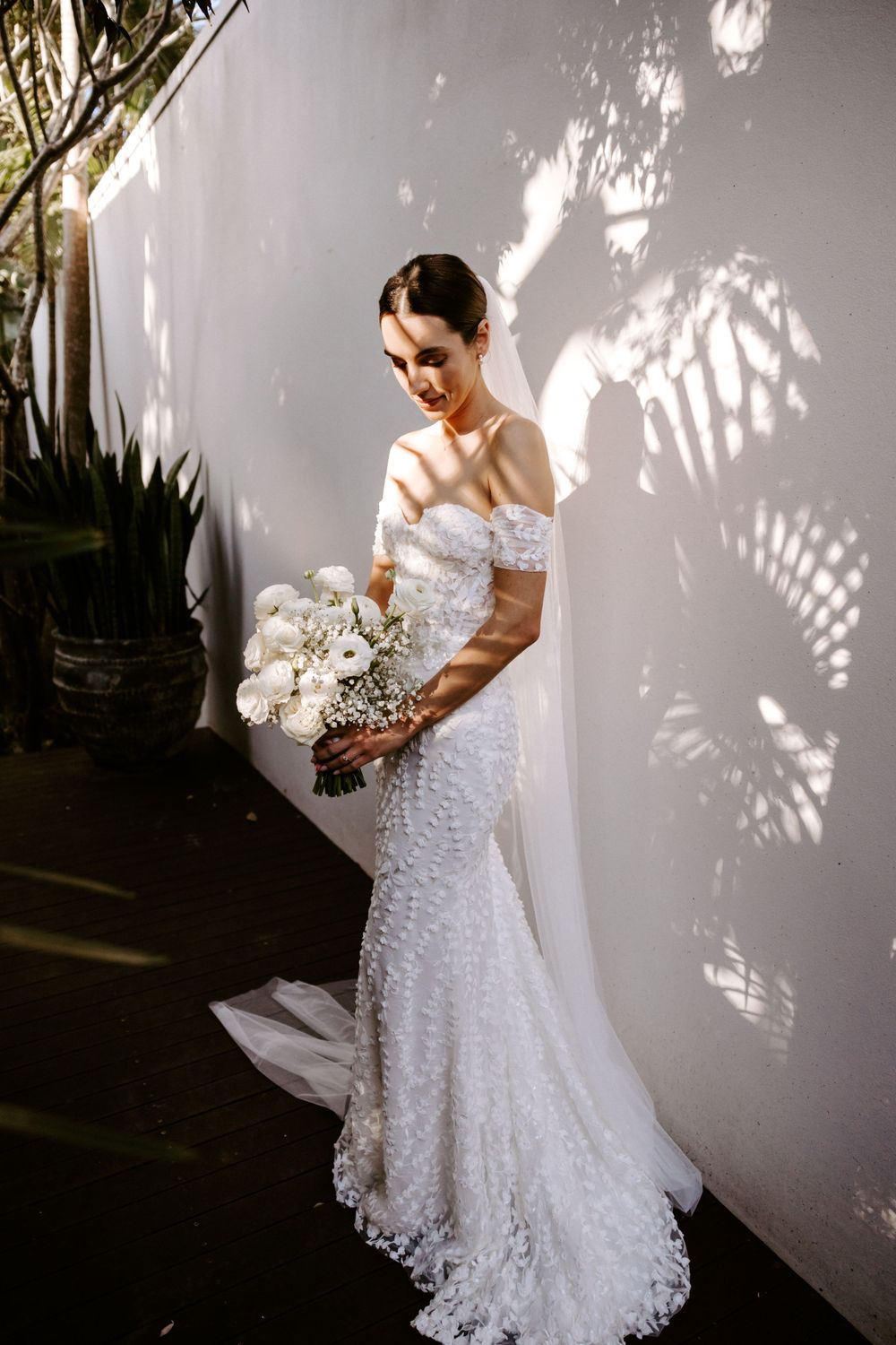 A romantic bridal portrait with sunlight casting shadows through tropical foliage.