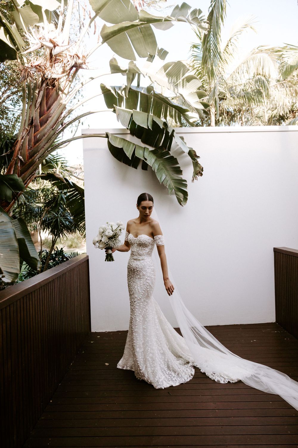 A classic bridal portrait with tropical foliage and white walls on a wooden deck.