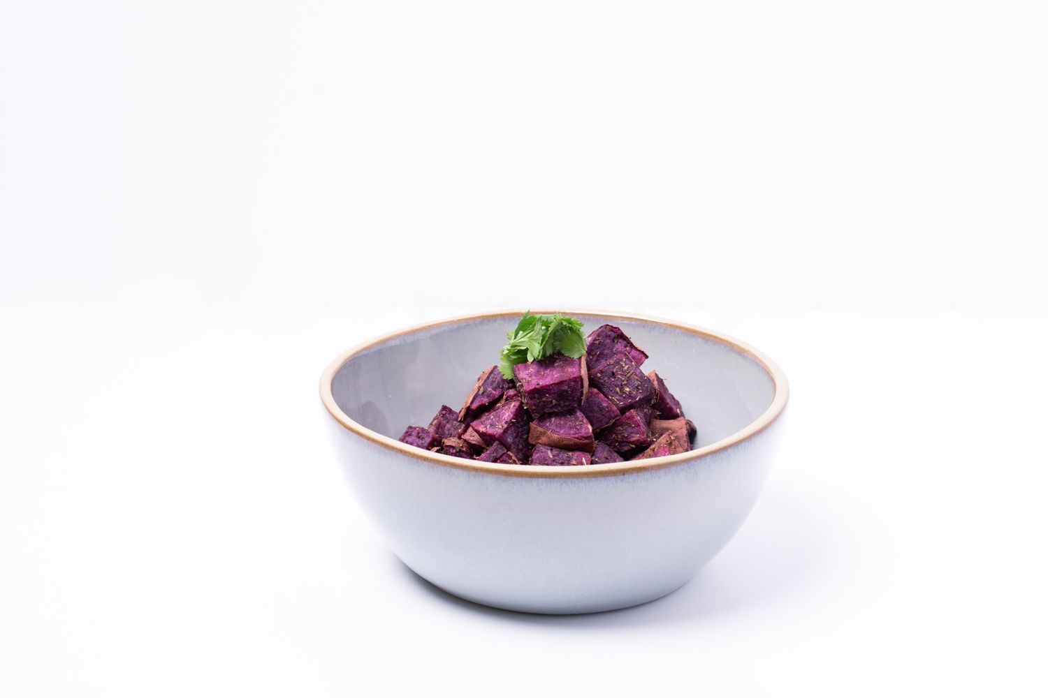 Cubed purple beets garnished with fresh herbs in a white ceramic bowl with gold rim.