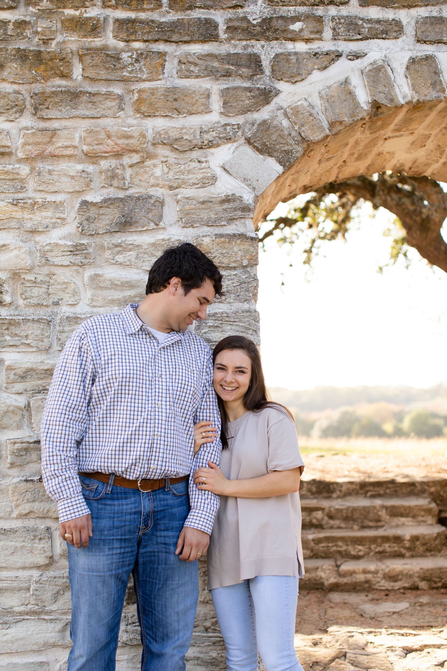 Couple sharing sweet moment under stone archway in casual attire.
