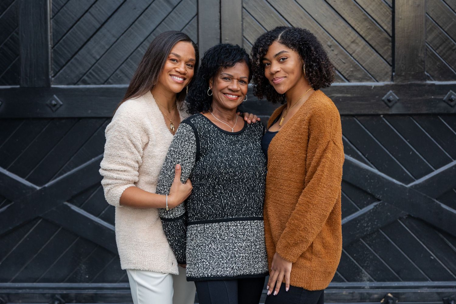Three friends pose together against a dark wall wearing casual outfits.