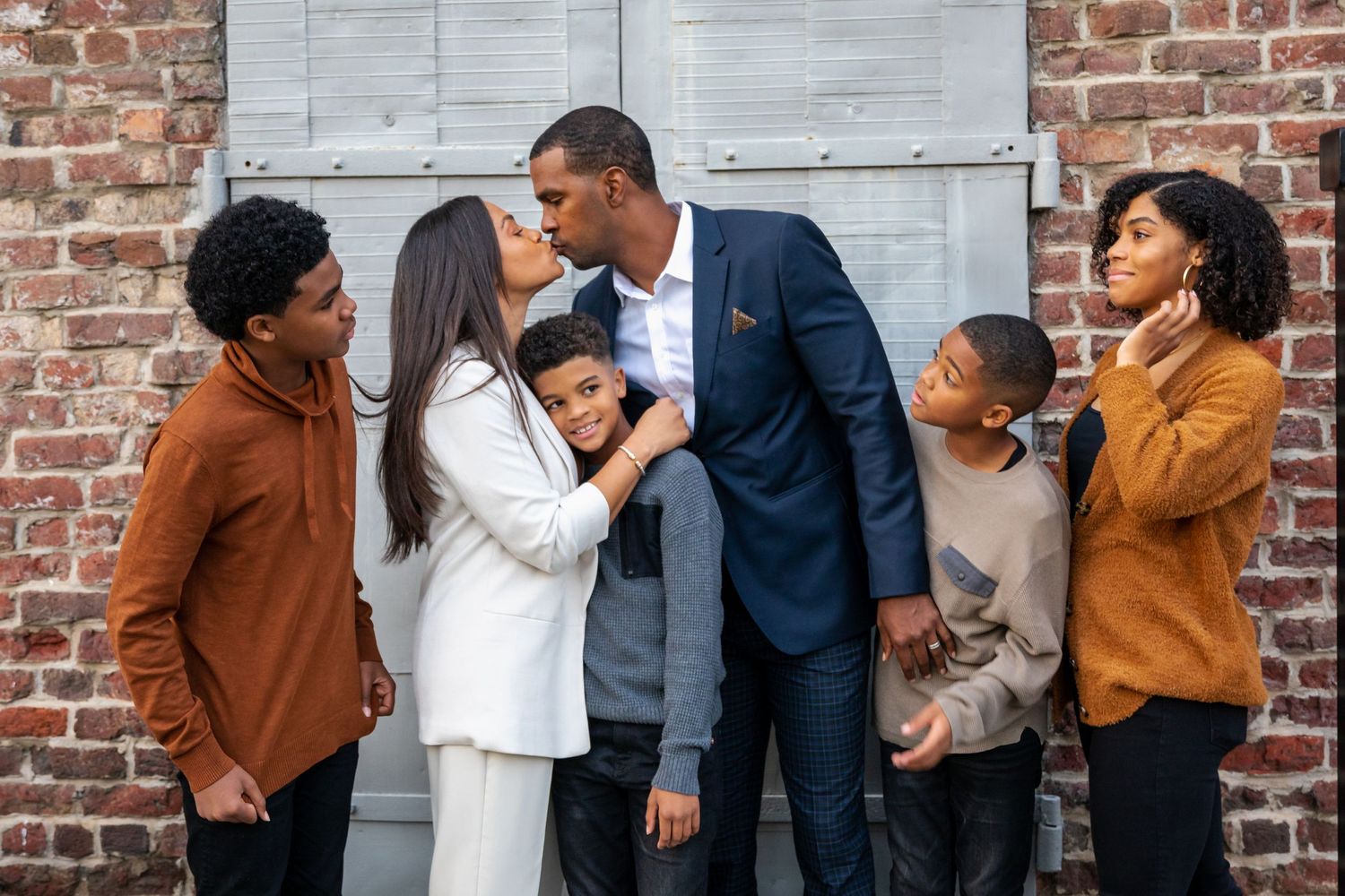 Family photo session against brick wall backdrop with coordinated brown and navy outfits.