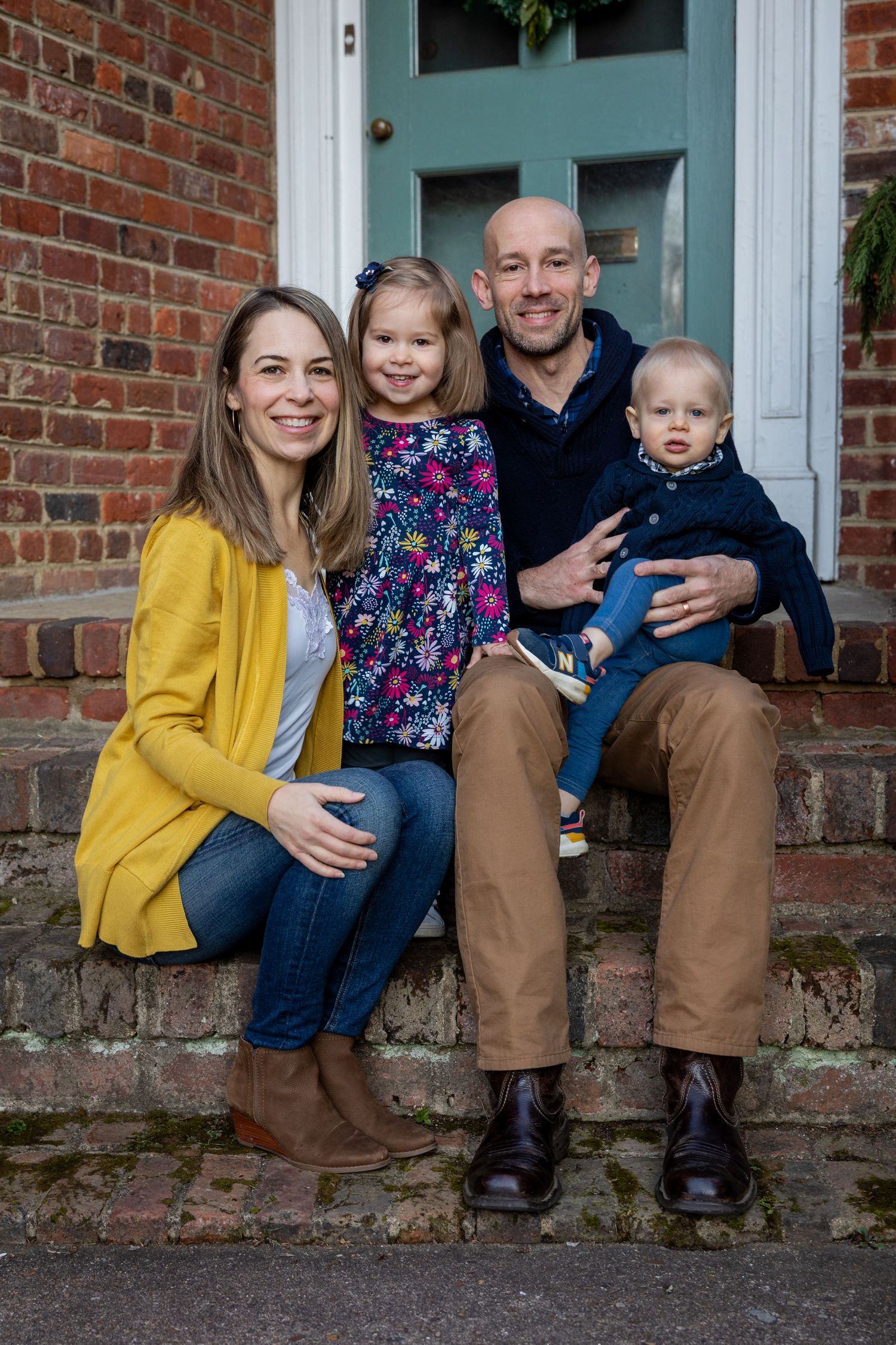 Family sitting together on brick steps in coordinated outfits with teal door background.