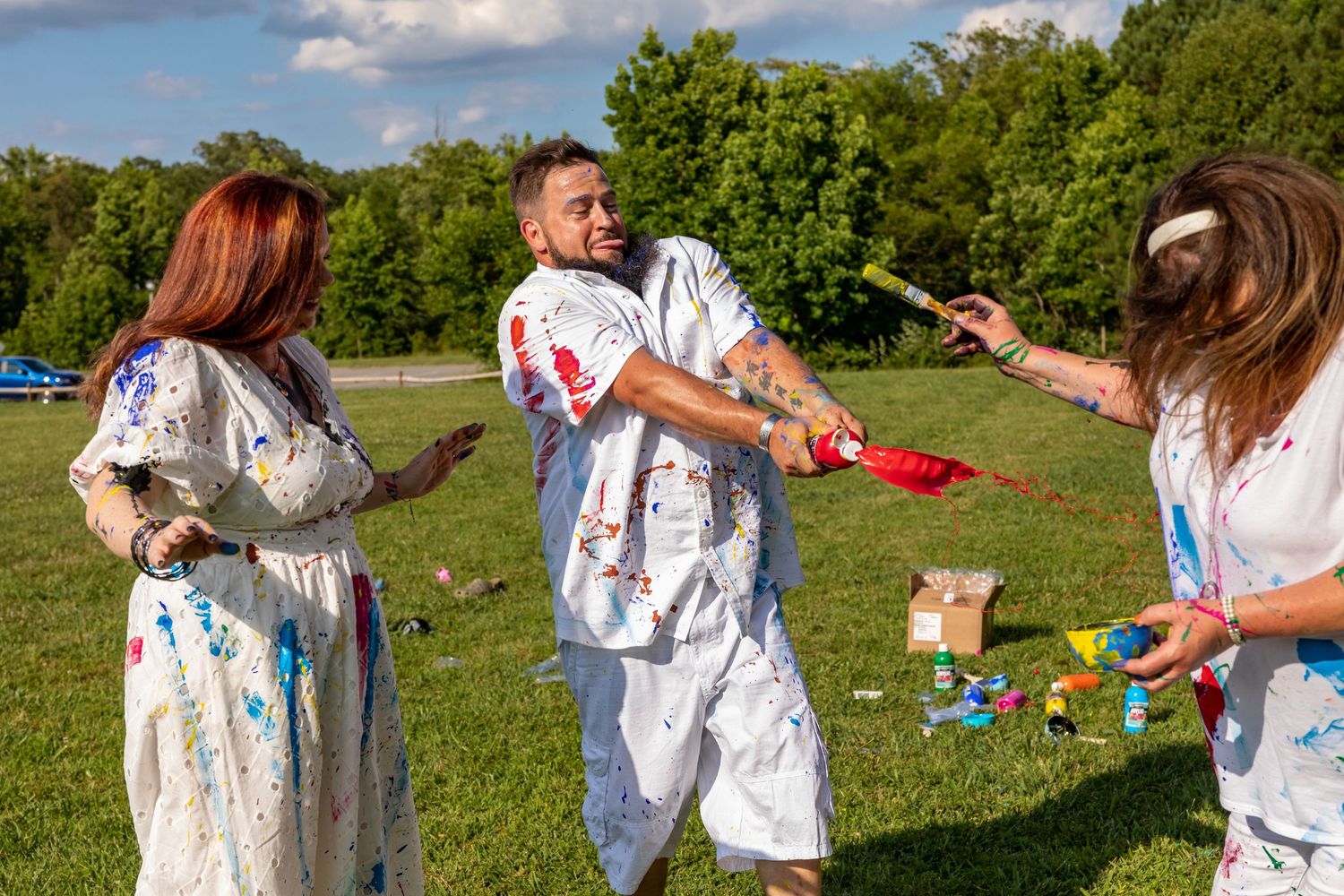 People in white t-shirts playing with colorful paint outdoors on a sunny day.