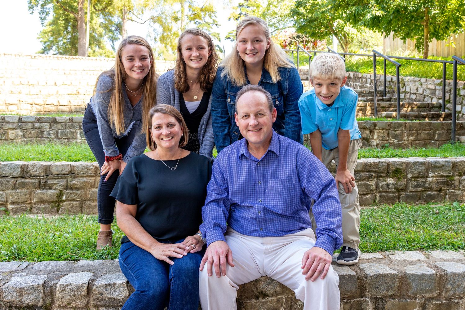 Multi-generational gathering on stone wall seating in a garden setting.