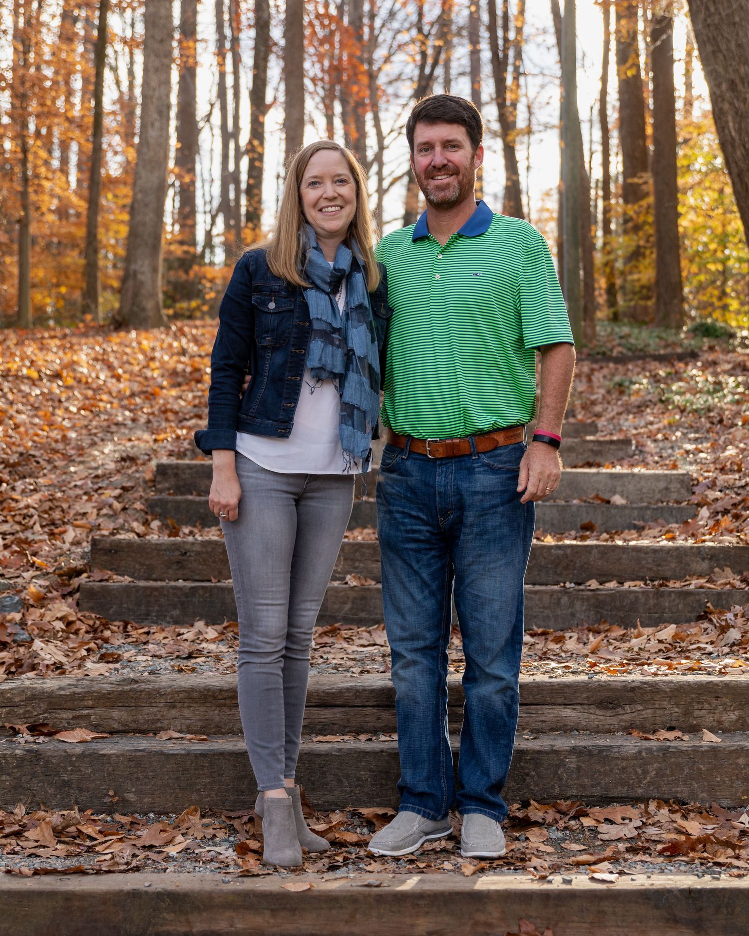 Couple walking down leaf-covered steps in autumn forest setting.